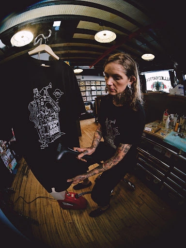 American Apparel campaign photograph of a creator holding a black printed T-shirt in a studio.