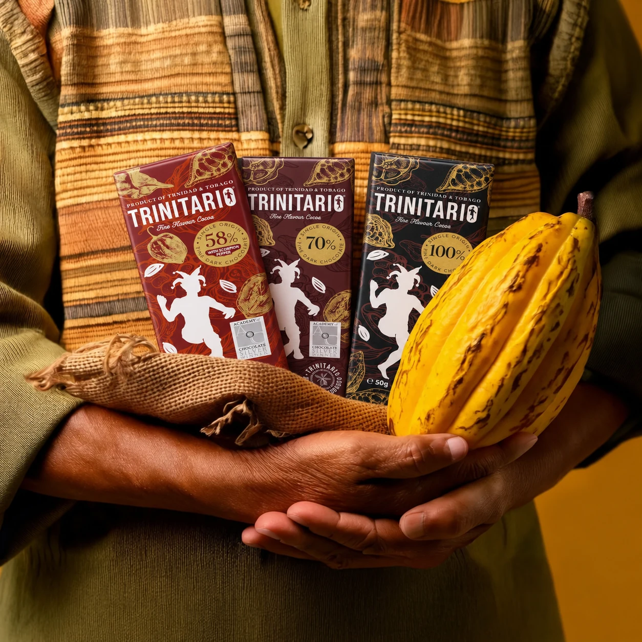 Three Trinitario bars showing 58% with Scorpion Pepper, 70% and 100% dark chocolate, held with a yellow cocoa pod.