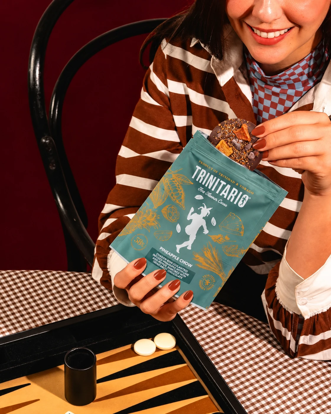 A Pineapple Chow medallion being taken from a turquoise Trinitario pouch beside a backgammon board.