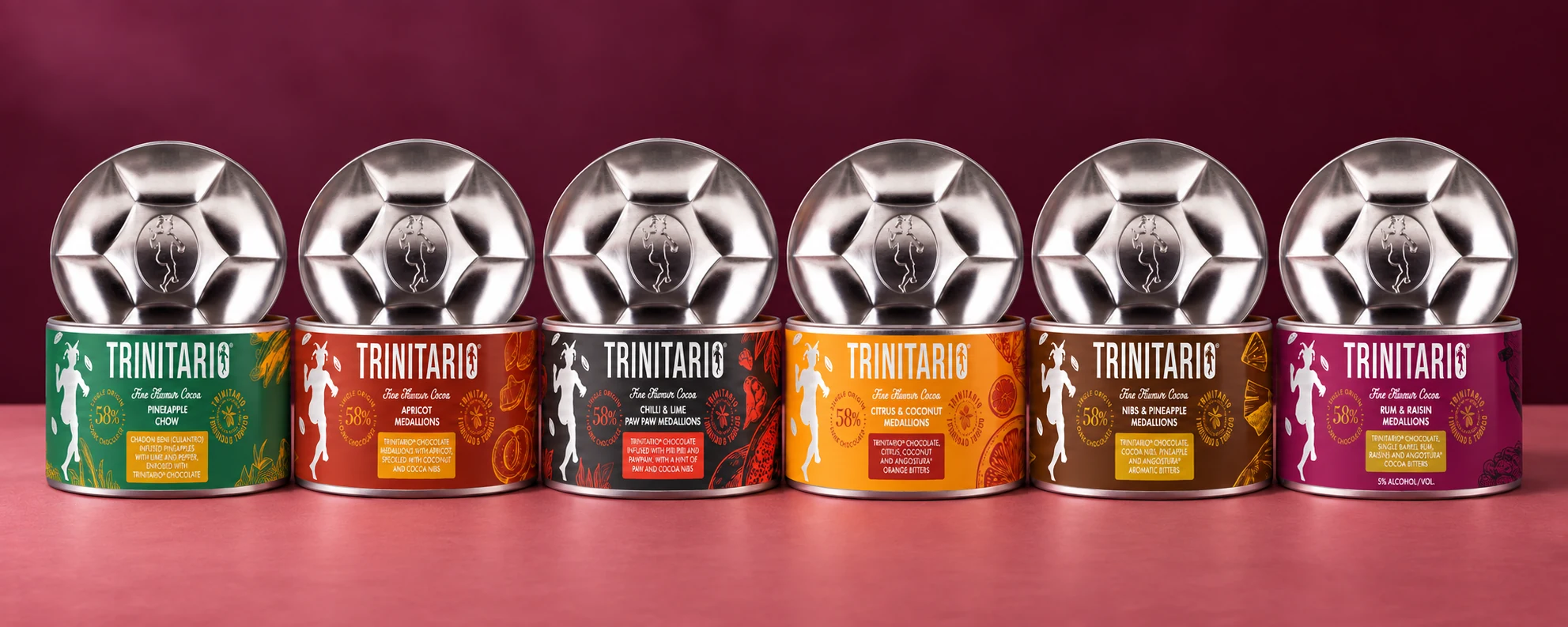 Six Trinitario tins with their steelpan-inspired silver lids: Pineapple Chow, Apricot, Chilli and Lime Paw Paw, Citrus and Coconut, Nibs and Pineapple, and Rum and Raisin.